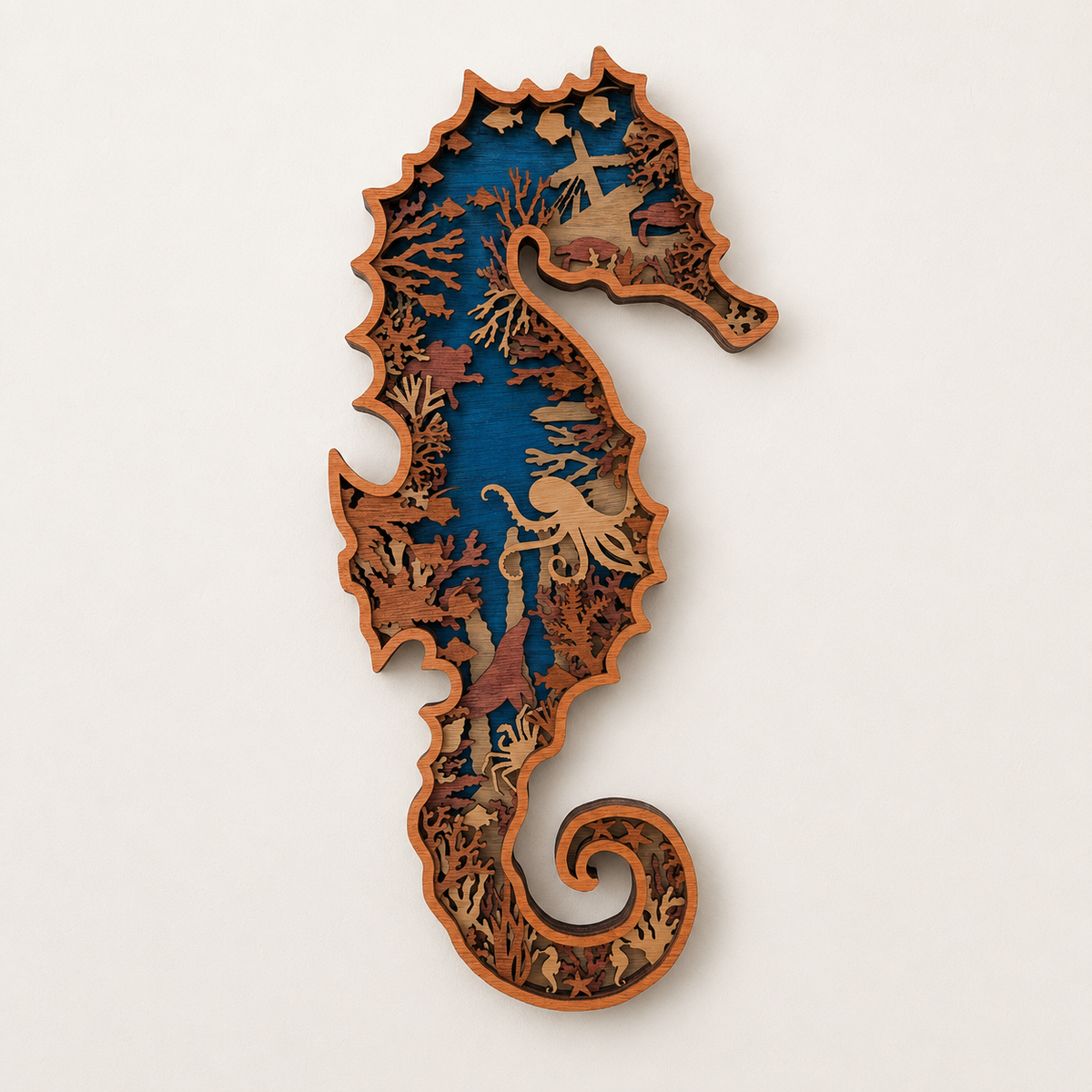 A seahorse-shaped wooden wall art piece with layered laser-cut details, featuring a blue background and natural wood sea life and coral patterns, shown against a plain off-white background.