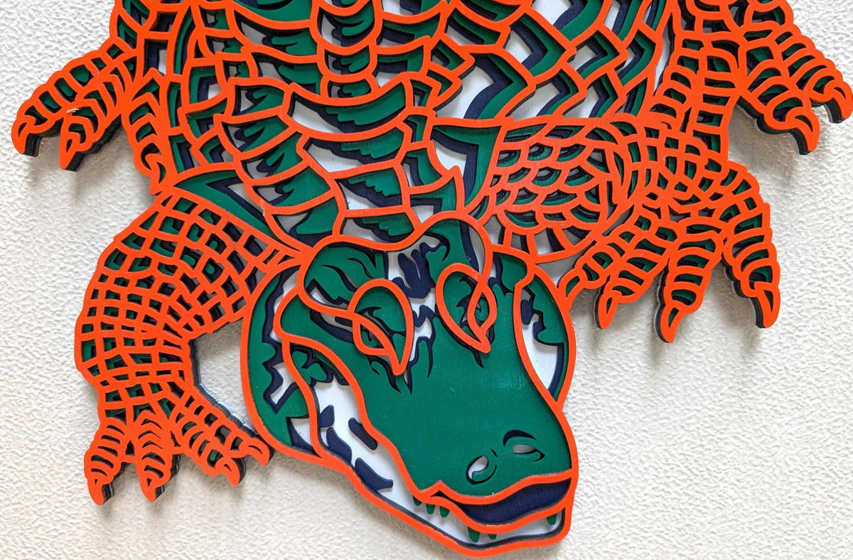 Layered Alligator Wall Art featuring a green alligator with orange outlined scales and navy, gray, and white wood layers